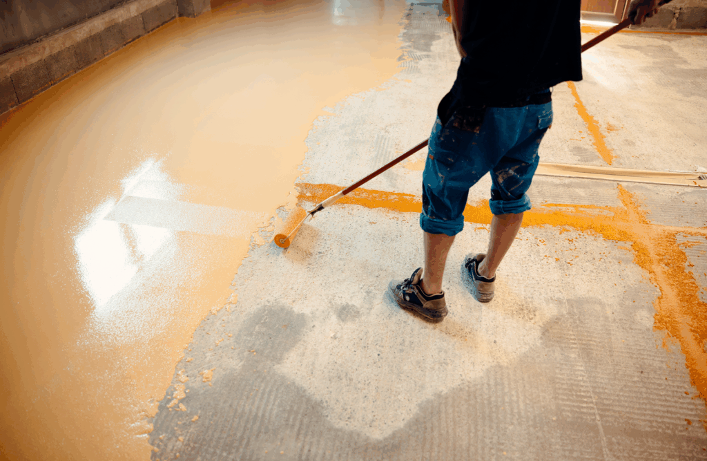 Pinturas Flores, Impermeaibilizaciones de alta calidad en Traiguera. Un trabajador impermeabilizando el suelo de una sala con resina naranja.