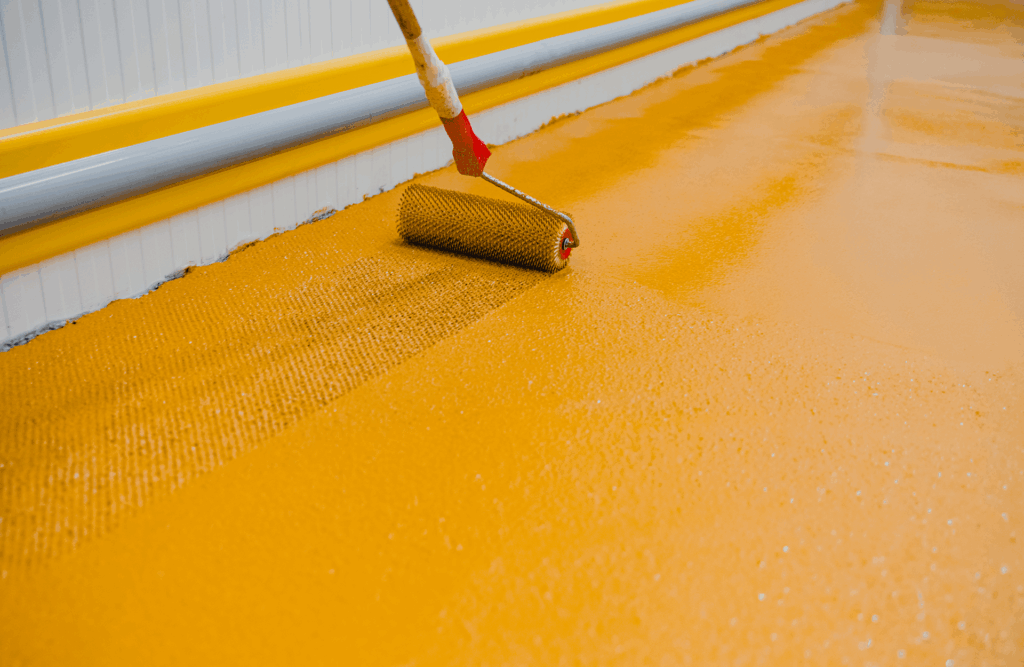 Pinturas Flores, pintores expertos de parkings y comunidades en Traiguera. Rodillo con pintura amarilla pasando por un suelo amarillo.