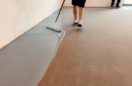 Pinturas Flores, Impermeaibilizaciones de alta calidad en Càlig. Un trabajador impermeabilizando el suelo de una sala con resina gris.