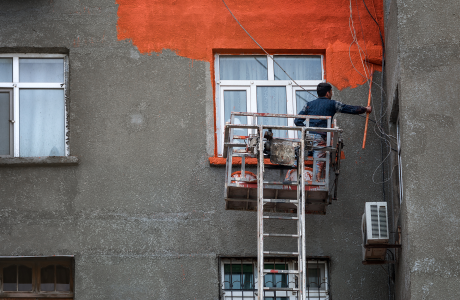 Pinturas Flores, Revestidores de fachadas cualificados en La Jana. Pintor pintando de naranja una fachada gris.